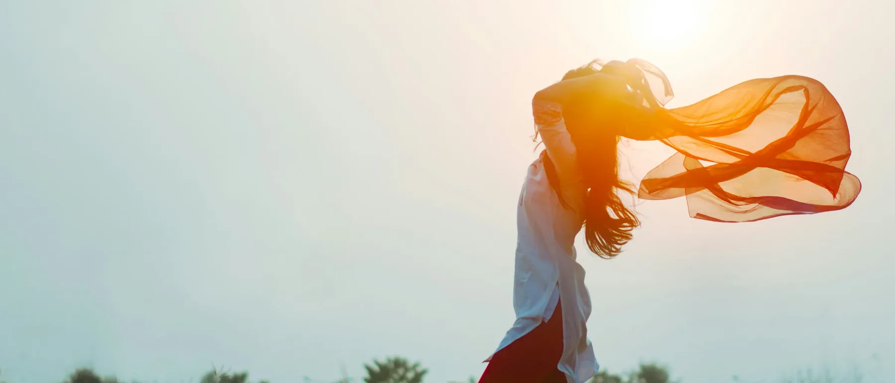 Mujer a contraluz con un pañuelo al viento, al atardecer