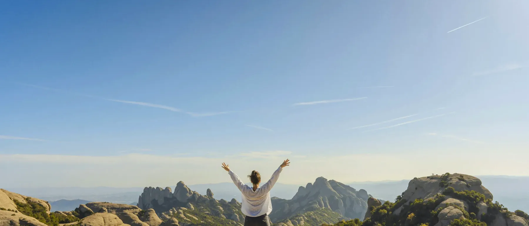 Mujer de espaldas, con los brazos abiertos, en la cima de una montaña
